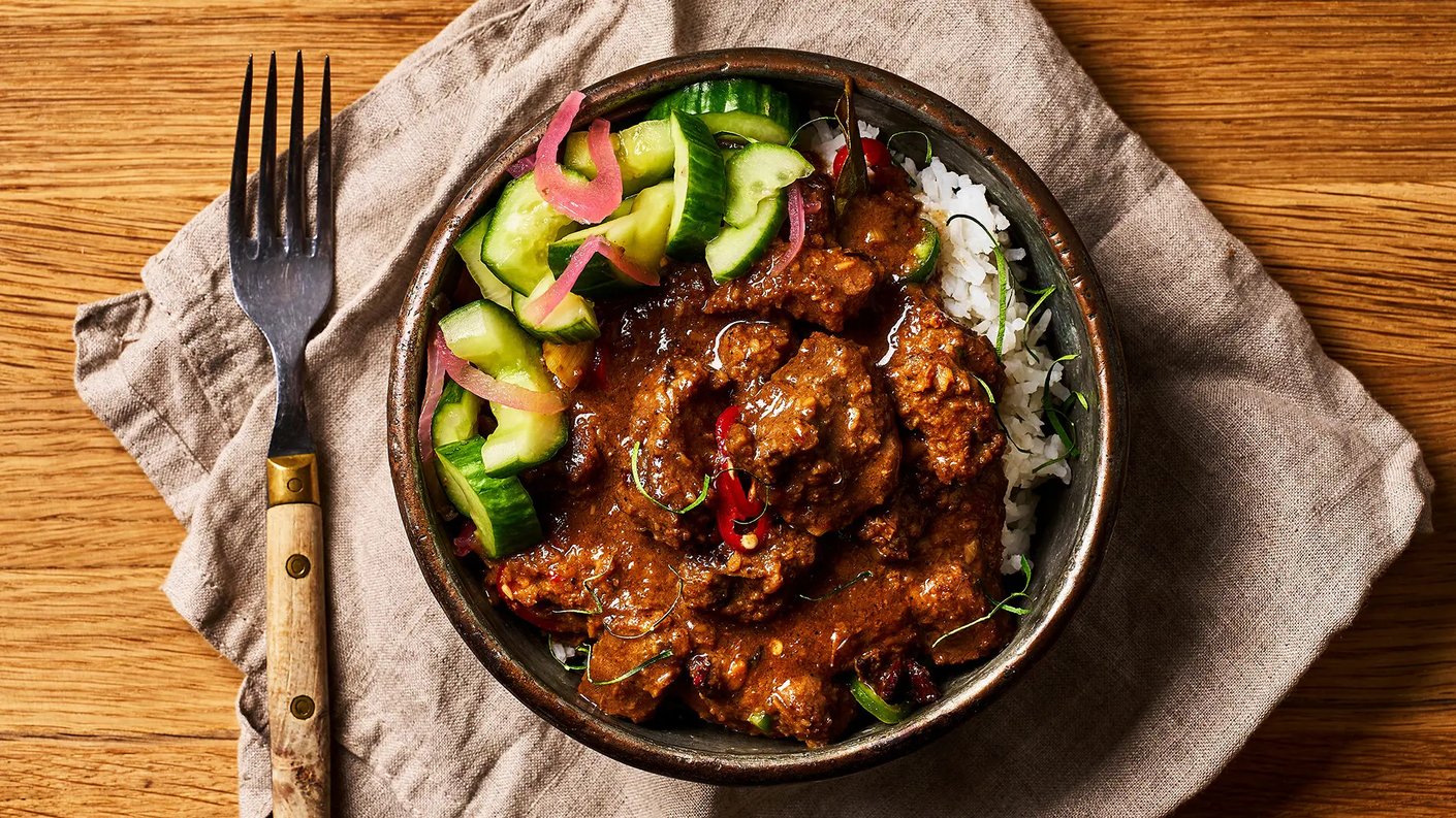 Rendang currya lautasella. Ohessa vihreitä kurkunpaloja ja pikkelöityä punasipulia.