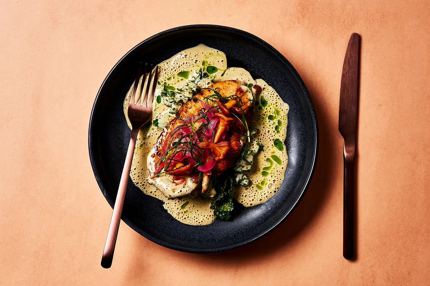 Mustalla lautasella tarjoiltu paistettu kananfileepihvi vaaleassa kermaviitakastikkeessa, koristeltuna marinoidulla punasipulilla, sienillä ja tuoreilla yrteillä.