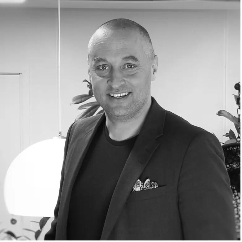 Mustavalkoinen, hymyilevä kuva Matti Karvosesta tumma pikkutakki ja t-paita päällään.päällään