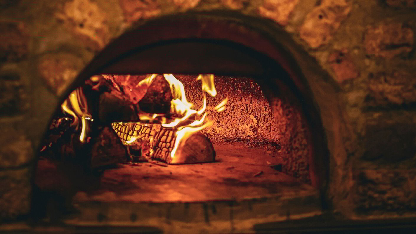 Kuva hehkuvasta puu-uunista. Uuni on yläosaltaan kaareva. Uunissa palaa useampi puu.