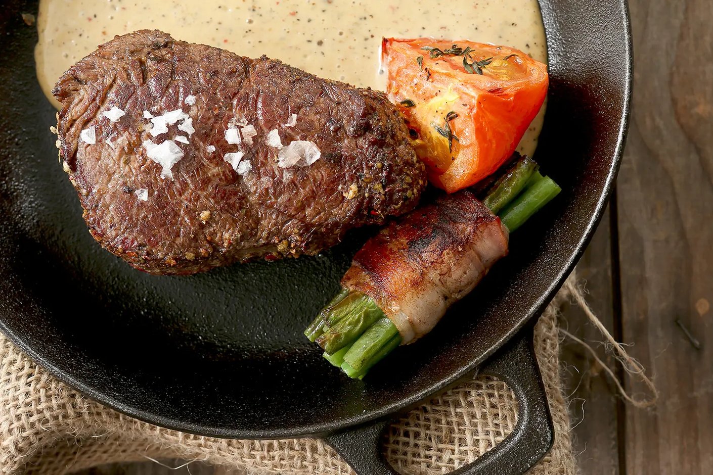 Valurautapannulla tarjoiltu pippuripihvi sormisuolalla, kermainen pippurikastike, paistettu tomaatti ja pekoninkääreeseen käärityt pavut.