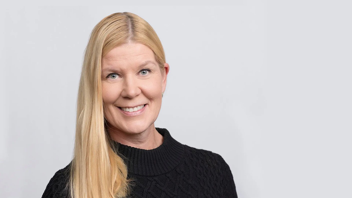 Mustapaitainen vaaleahiuksinen Soile Käkönen hymyilee kuvassa harmaata taustaa vasten.