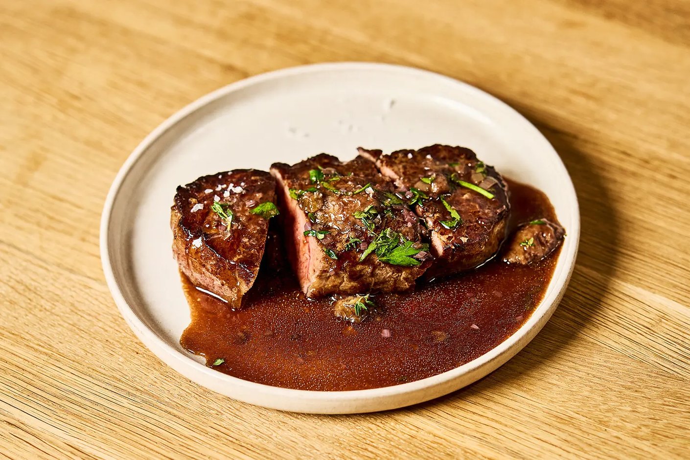 Paistettu naudan marmorifilee leikattuna viipaleiksi tummassa Espagnole-kastikkeessa, päällä sormisuolaa ja tuoreita yrttejä.