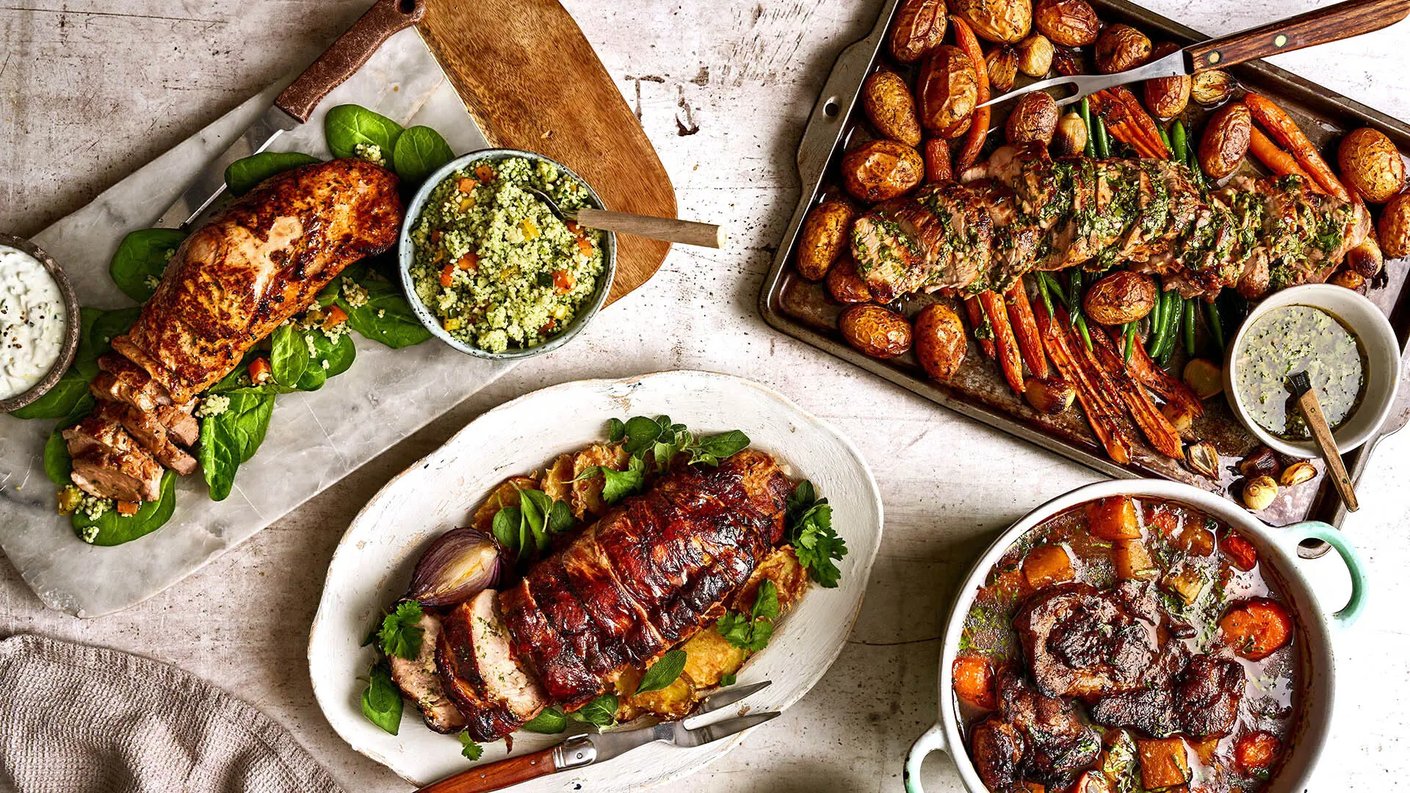 Ylhäältä otettu, visuaalisesti runsas kuva useista erilaisista, kauniisti esille asetetuista liharuokalajeista ja lisukkeista, jotka luovat vaikutelman runsaasta juhla-ateriasta tai viikon ruokalistaesittelystä.