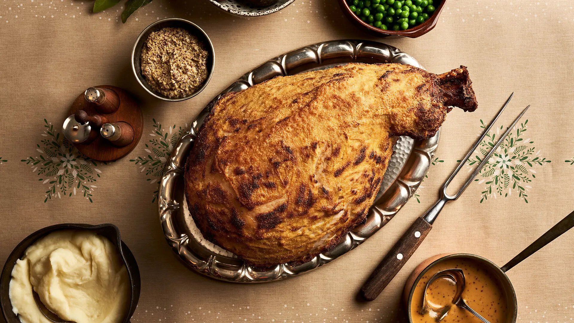 Paistivadilla kokonainen paistettu joulukinkku, vieressä sinappia, herneistä ja kastiketta. 